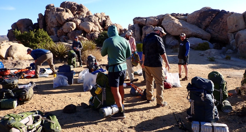 a group of veterans backpacking in joshua tree take a break among large rock formations